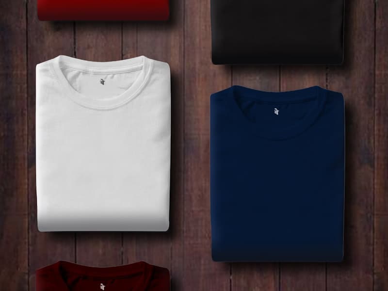 Folded white and navy T-shirts arranged on a dark wooden surface
